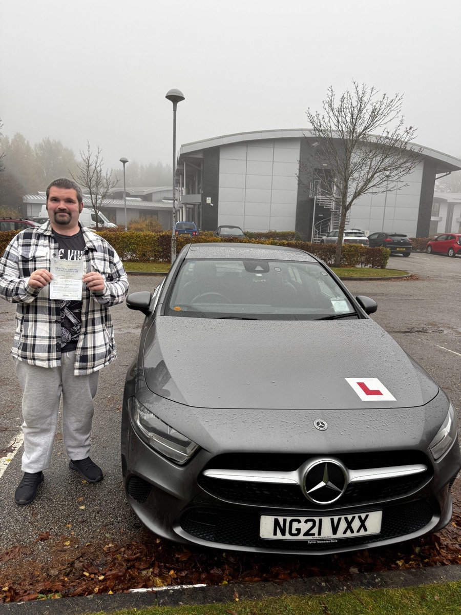 Blue Drive pupil holding a pass certificate beside the Mercedes-Benz training car